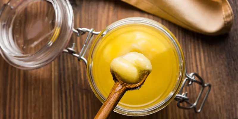 spoon of ghee taken from a glass jar full of ghee