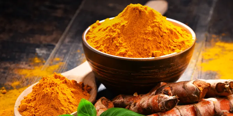 turmeric powder in a wooden bowl along with a spoonful of turmeric powder