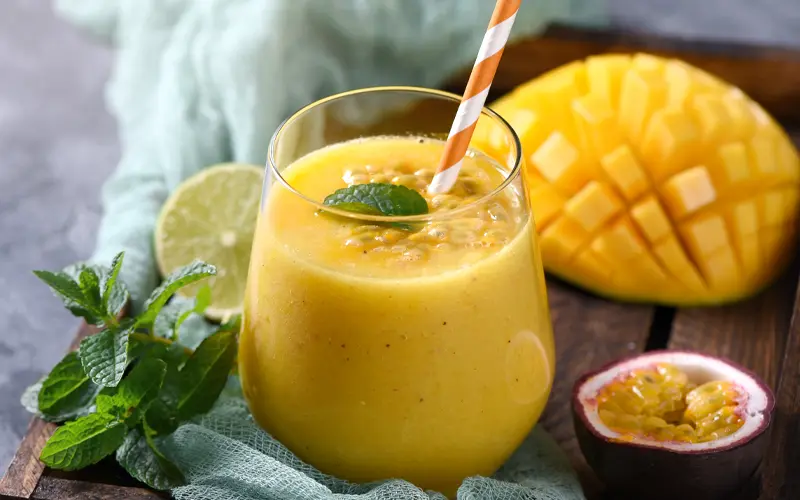 Spicy Mango drink in a glass on table with mango pieces behind