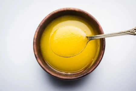 Ghee or clarified butter close up in wooden bowl and silver spoon