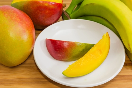 Mango fruit slices on saucer among mango and bananas